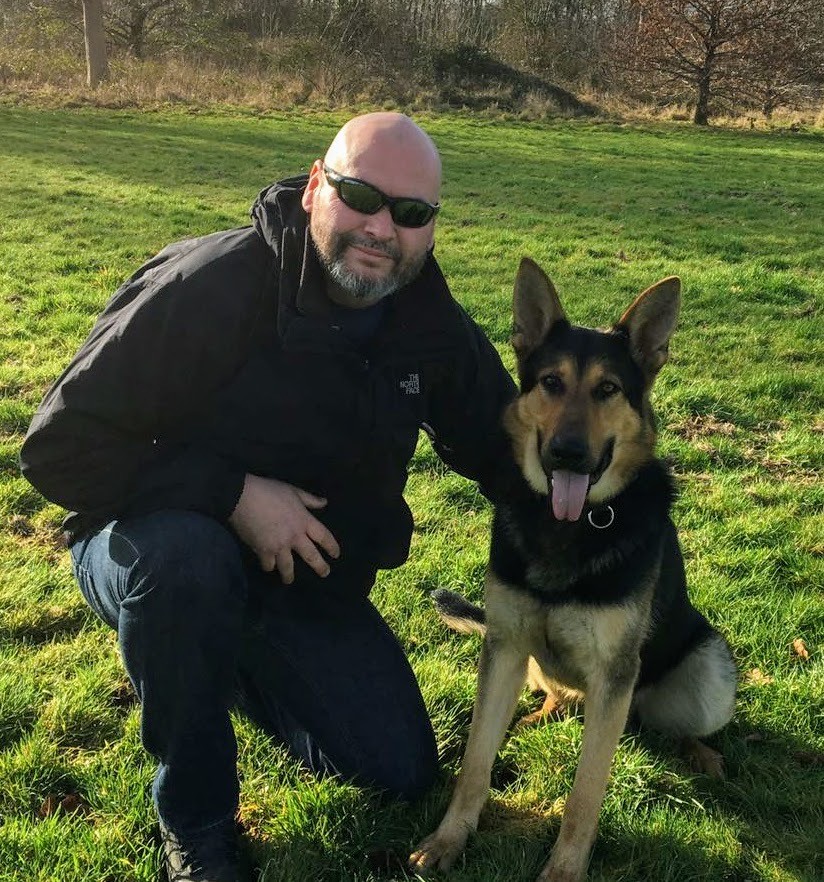 David with a German Shepherd sitting calmly at his side in a field.